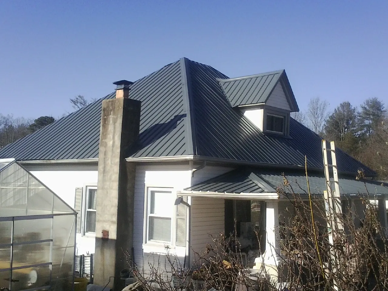 Dark blue standing seam metal roof on a white farmhouse with dormer — Slate & Tile Roof Repair by Roofing Brothers in Elk Horn