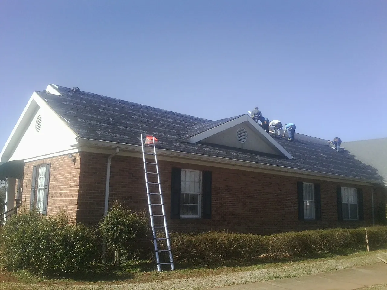 Crew tearing shingles off a brick ranch roof with a ladder set — Emergency Roof Repair work by our crew in Elk Horn