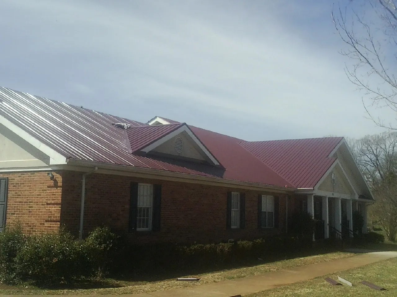 Red metal roof with gabled entries on a long brick building, from a Hail Damage Roof Repair job in Elk Horn