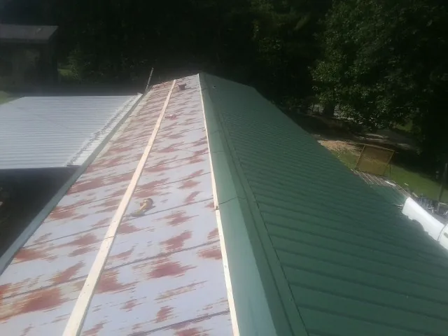 Old rusted panels beside newly installed green metal roofing — Wind Damage Roof Repair by Roofing Brothers in Elk Horn
