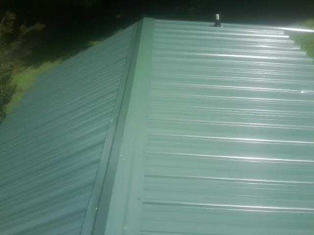 New green metal panels meeting at the ridge of a roof — Flat Roof Repair work by our crew in Elk Horn