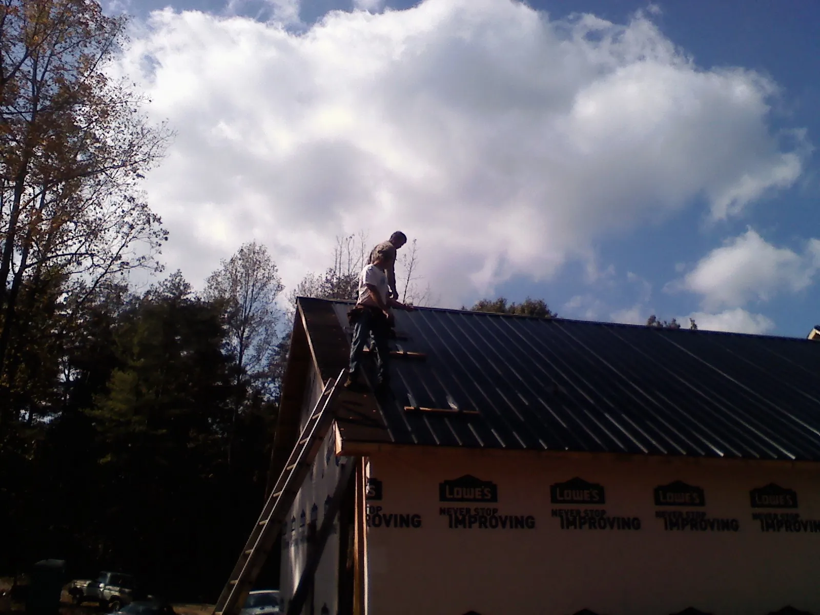 Roofer fastening dark metal panels high against a cloudy sky, from a Roof Inspection job in Elk Horn