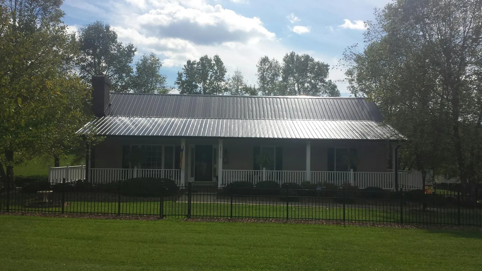 Gray metal roof on a brick ranch with a full width front porch — Gutter Guard Installation work by our crew in Elk Horn