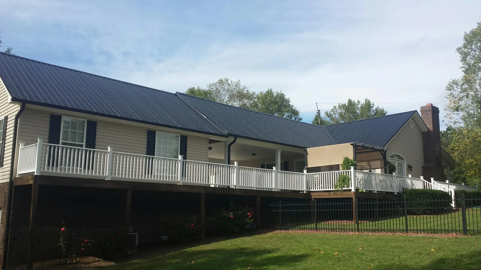 Black metal roof above a long white railed deck on a hillside home in Elk Horn