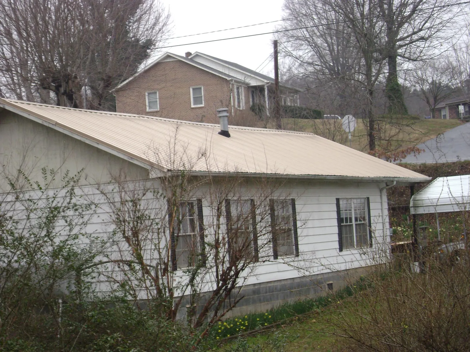 Tan metal roof on a white sided house set into a hillside — Commercial Roofing by Roofing Brothers in Elk Horn
