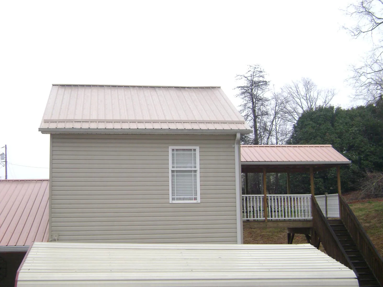 Tan metal roofs on a two story addition and attached porch, from a Roof Replacement job in Elk Horn